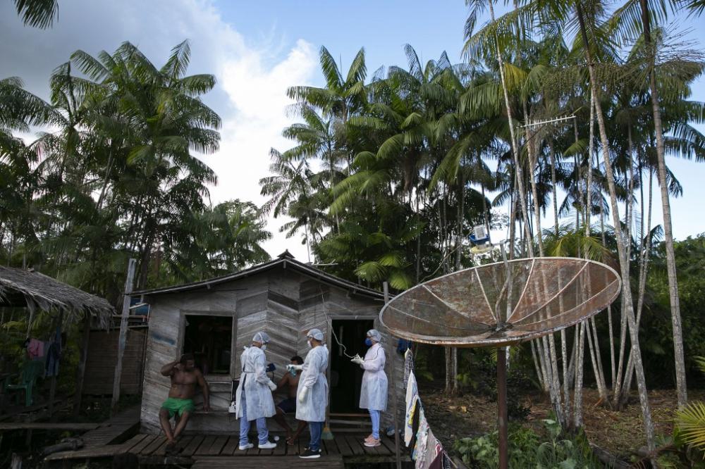 Government health workers take the temperature of a patient as they visit riverside communities of the municipality of Melgaco to test them for COVID-19 coronavirus infections in the Marajoara region, located in the southwest of the island of Marajo, at the mouth of the Amazon River in the state of Para, Brazil, on May 23, 2020. By Tarso Sarraf / AFP.