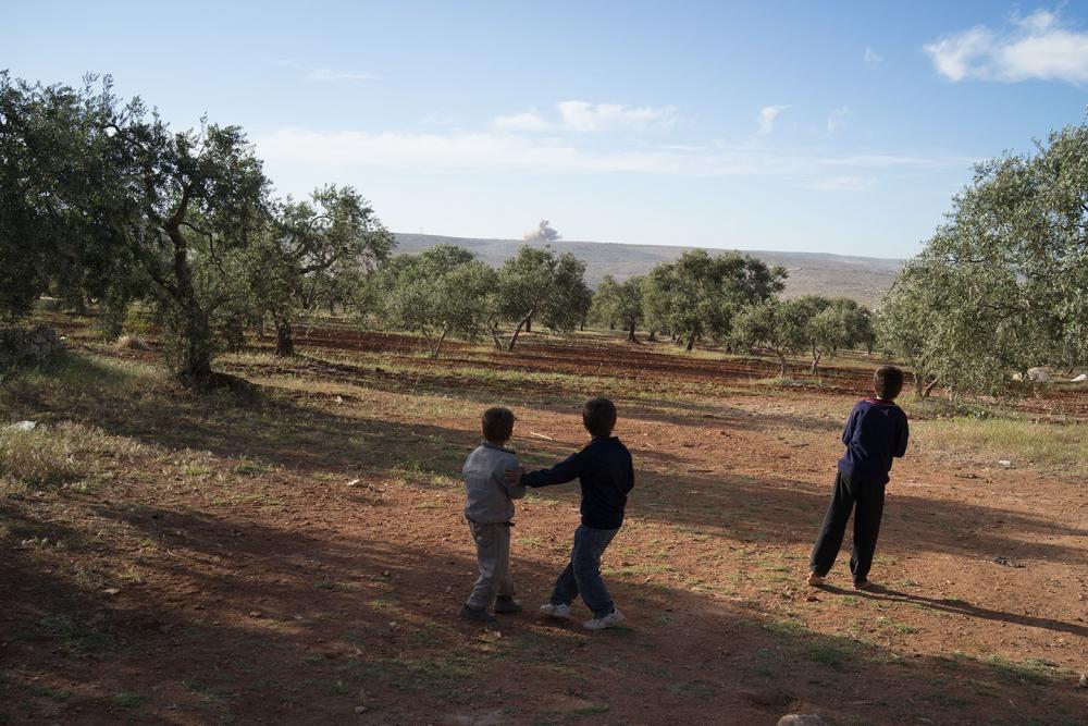 The internationally recognized photographer Matthias Bruggmann took this image in Haas, Reff Idlib, Syria, on 1 May 2014. Of this scene suspended in time, Bruggman states: "these children are watching an airstrike on Shinshirah, one of the "dead cities" UNESCO world heritage site." This photograph is part of the book "An Act of Unspeakable Violenc